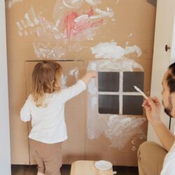 A father and his daughter paint a playhouse made of cardboard.