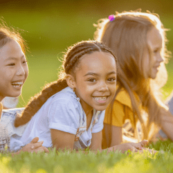 A handful of smiling kids lay on their stomachs on the grass.