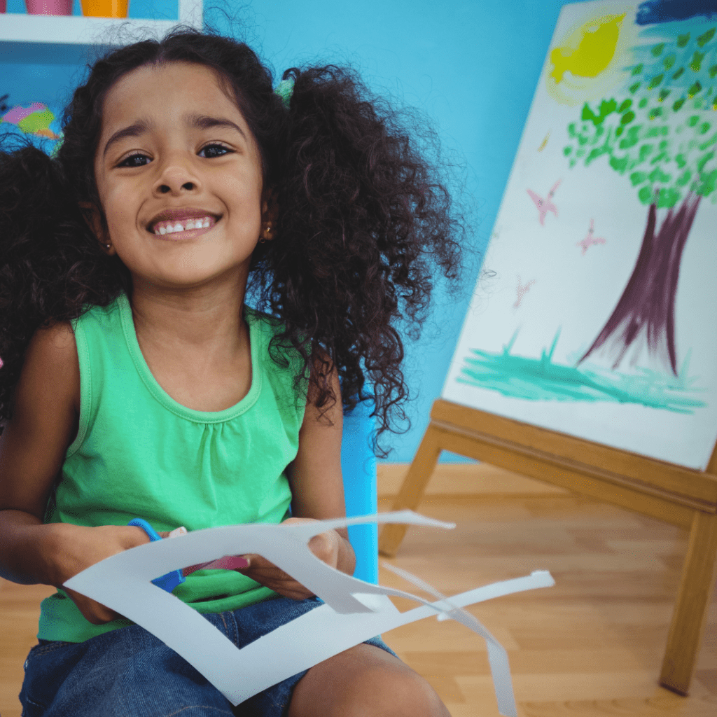 A child holds paper and scissors next to an easel.