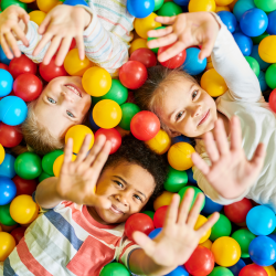 Three kids lay in a ball pit, holding up their hands.