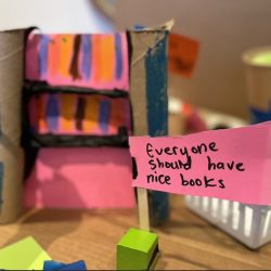 A cardboard craft bookshelf with a paper flag in front that reads: Everyone should have nice books.