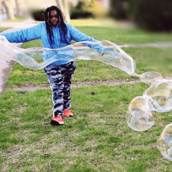 Child using giant bubble blower in the yard.