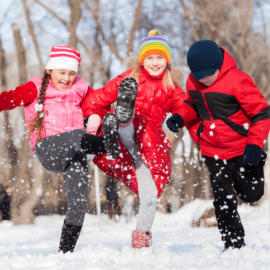 Three kids in winter gear kicking up snow.