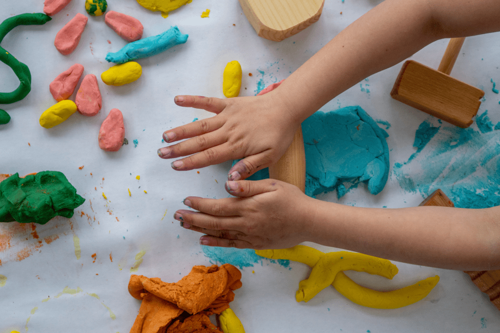 Close up of child's hands rolling play dough with small wooden rolling pin.