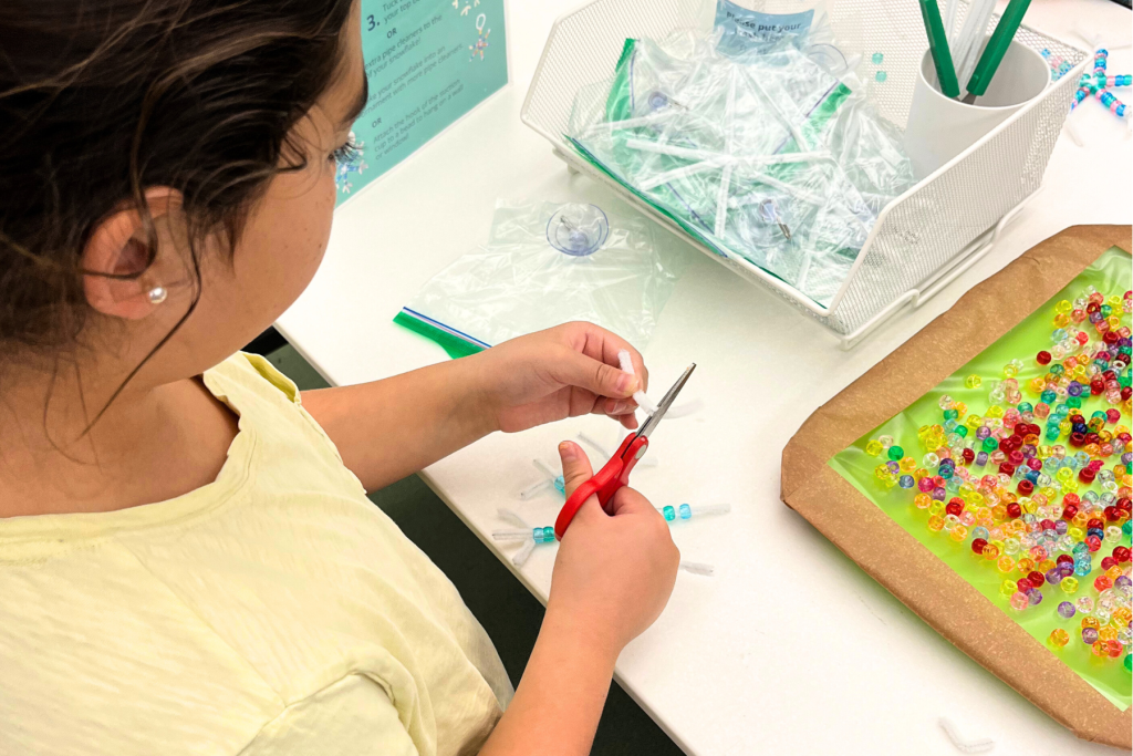 Girl putting together a craft with pipe cleaners and beads.